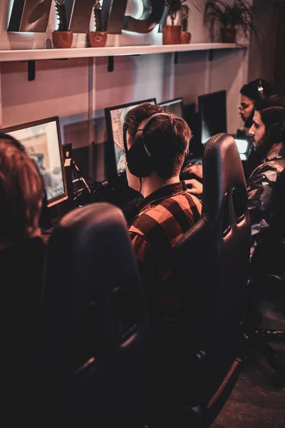 Players seen from behind at a row of monitors along a shared desk in a warm-lit club